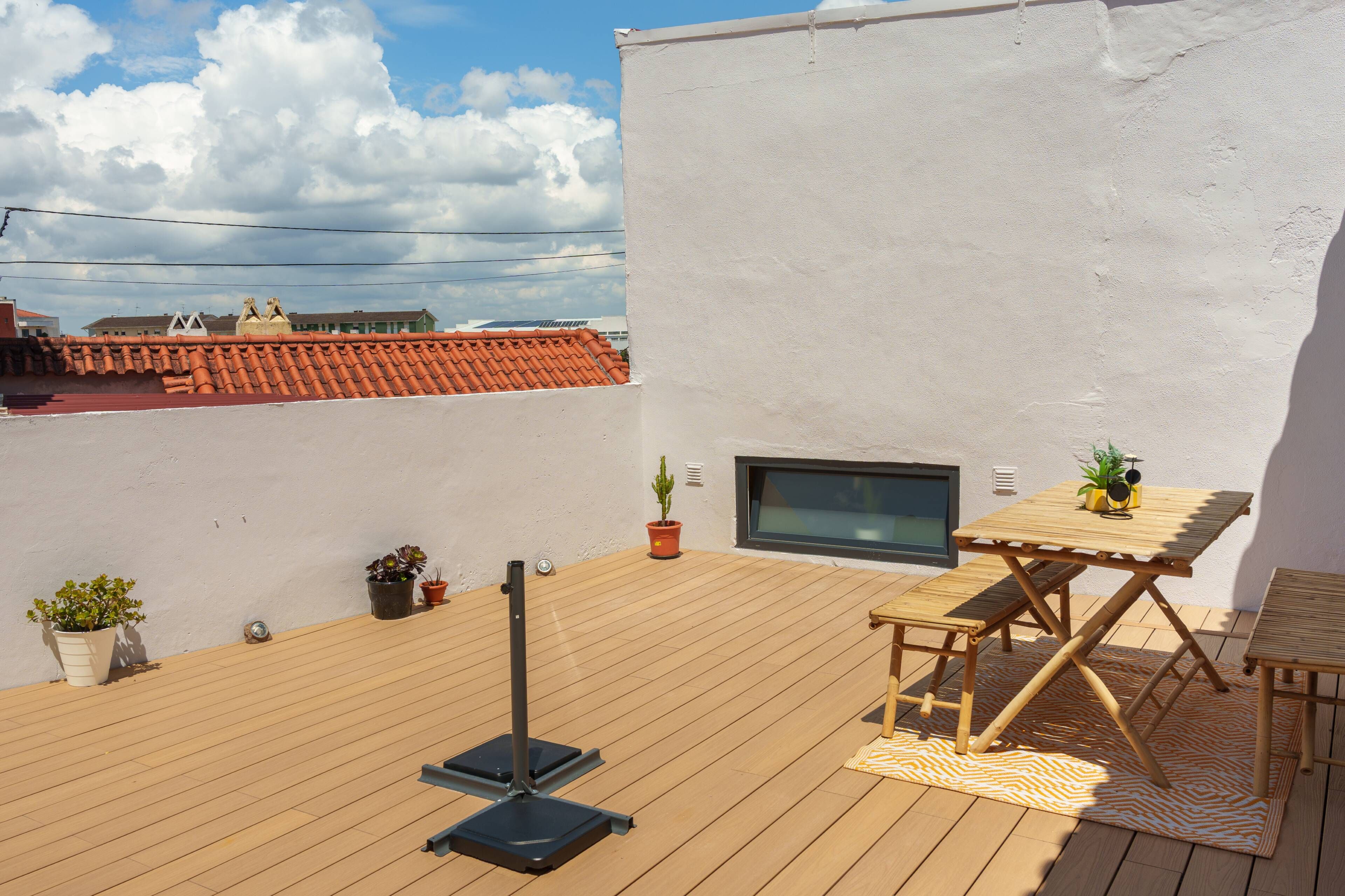 Una terrazza sul tetto con un pavimento in legno, un tavolo con sedie e piante in vaso.