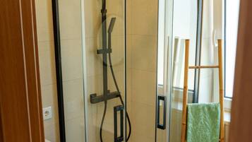 A glass-enclosed shower with a control panel, a wooden cabinet, and a green towel on a wooden chair.