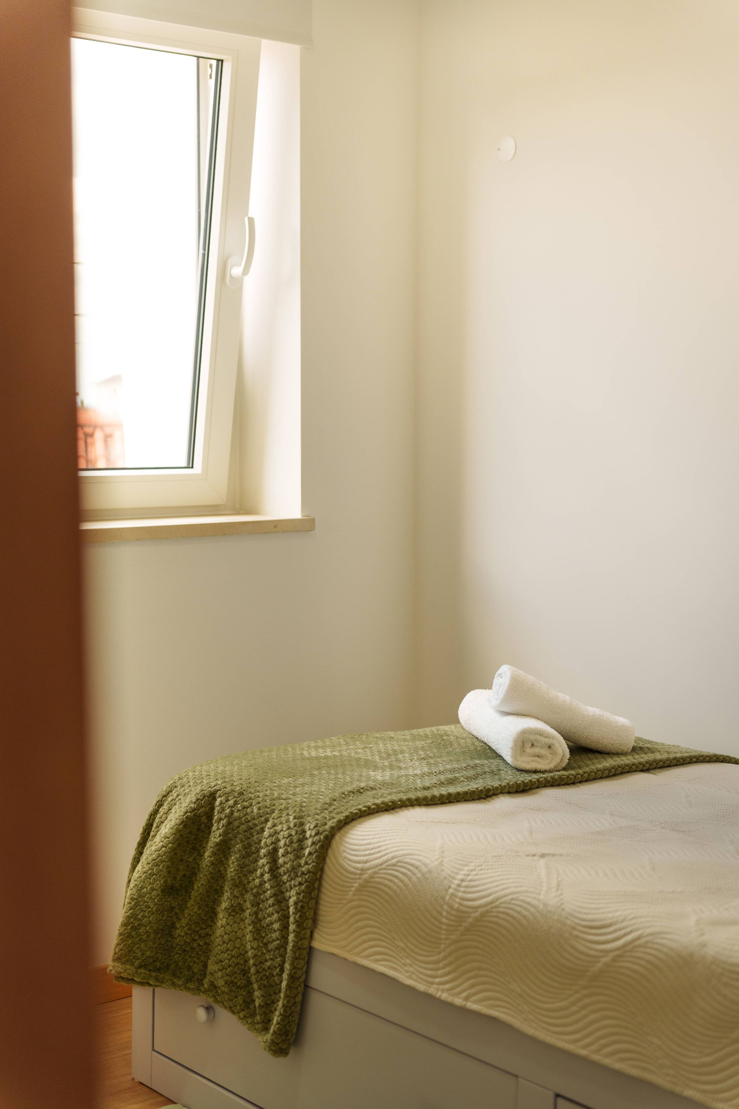 Une chambre avec un lit simple, une fenêtre et une couverture verte.