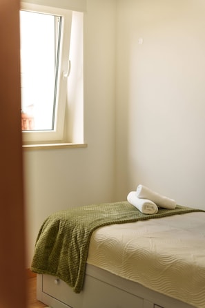 Un dormitorio con una cama individual, una ventana y una manta verde.
