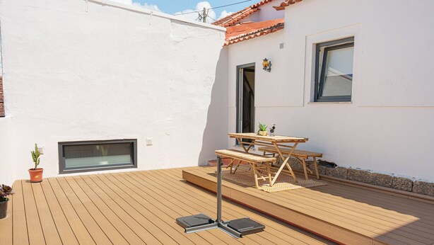A wooden deck with a table and chairs, a potted plant, and a window. - Stay at SuCaSa in Coimbra (Coimbra)