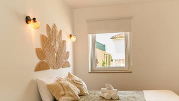 A bedroom with a bed, a window, a wall-mounted light fixture, and a small stool.