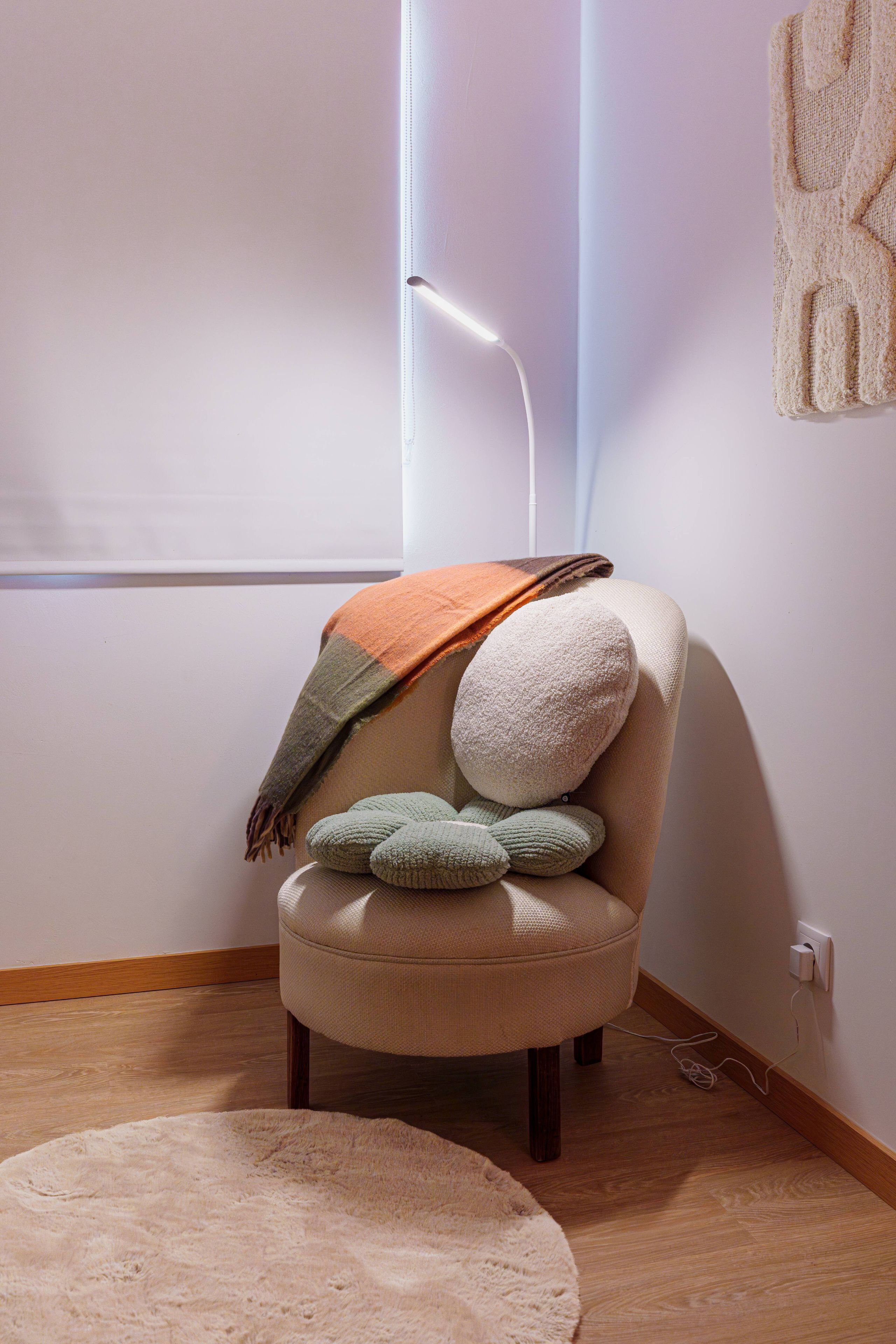 Ein Sessel mit Decke und Kissen, eine Lampe und ein Teppich in einem Raum mit Holzboden und einer Steckdose.