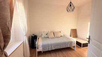 A bedroom with a bed, a hanging light fixture, a door, and a window with curtains.