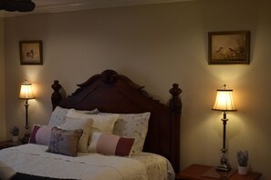 A bedroom with a large wooden bed, two bedside lamps, a framed picture on the wall, and a small table with a lamp and a plant. - 3-bedroom house in The Colony near Grandscape (The Colony)