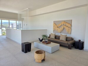 A modern living room with a sofa, coffee table, and a large window overlooking a cityscape. - Vrbo Property (Bucerías)