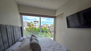 Et soveværelse med seng, fjernsyn på væggen og en balkon med udsigt til bygninger.
