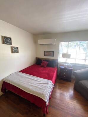 A bedroom with a bed, a nightstand, a lamp, and a window with blinds. - Bright and Cozy Studio Retreat with Classic Dallas Charm (Dallas)