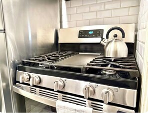 A stainless steel gas range with four burners, a digital control panel, and a kettle on the stove. - Bright and Cozy Studio Retreat with Classic Dallas Charm (Dallas)