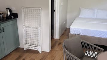 A room with a bed, a chair, a table, a kitchenette, and a door leading to another room.