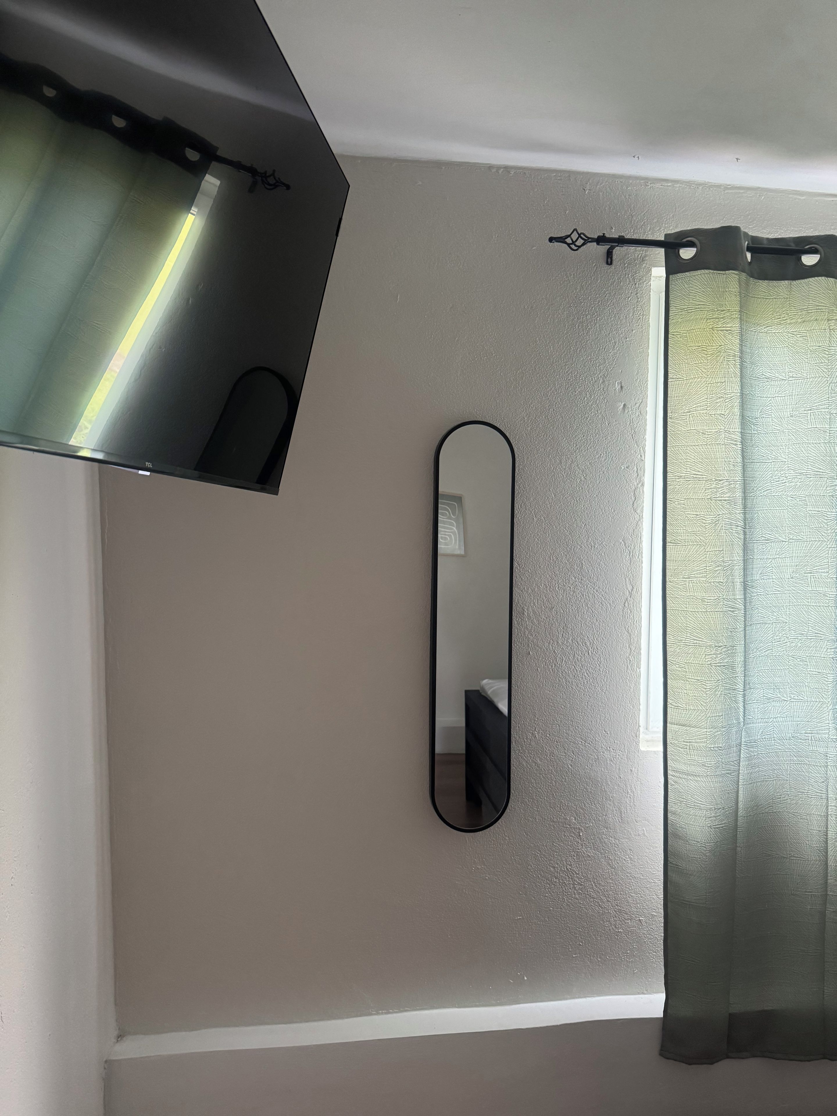 Quarto com cama, espelho fixado na parede e janela com cortina.