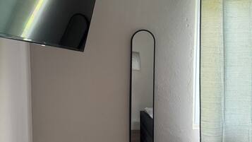Quarto com cama, espelho fixado na parede e janela com cortina.