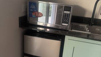 Cozinha compacta com micro-ondas, mini-geladeira e pia.