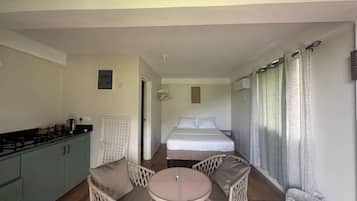 A compact room with a kitchenette, a bed, two chairs, a small table, and a window with curtains.