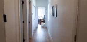 Ein Flur mit Schreibtisch und Stuhl, einer Tür links sowie gerahmten Bildern an der Wand.