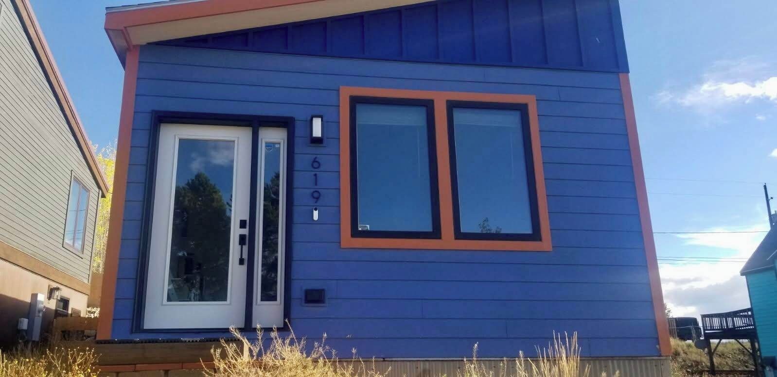 Una casa azul con puerta blanca y dos ventanas, se observa el número 610.