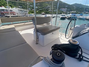 A boat deck with a cushioned seating area, a steering wheel, and a coiled rope. - EXCLUSIVE OFFER! 46' Luxury Catamaran Yacht with free access to 5 Star Resort! (Key West)