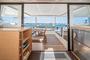 A boat's interior with a dining area, wooden shelves, and a view of the marina. - EXCLUSIVE OFFER! 46' Luxury Catamaran Yacht with free access to 5 Star Resort! (Key West)