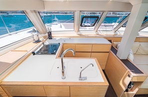 Das Interieur einer Yacht mit Küchenbereich, einschließlich Spüle und Schränken, und Blick auf den Hafen durch große Fenster.