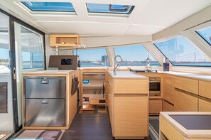 A compact galley with a refrigerator, microwave, sink, and wooden cabinetry. - EXCLUSIVE OFFER! 46' Luxury Catamaran Yacht with free access to 5 Star Resort! (Key West)