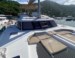 Eine Yacht mit überdectem Deck, Sitzgelegenheiten und Blick auf den Hafen sowie die dahinter liegenden Hügel.