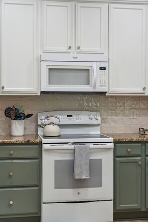 A kitchen with white cabinetry, a microwave, an oven, and a kettle on the countertop. - Seaglass! Folly 30 night Minimum Stay-Close to Beach & Town- (Folly Beach)