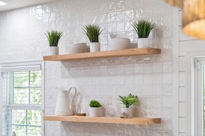 A bathroom with white tiled walls, wooden shelves, and various toiletries. - Seaglass! Folly 30 night Minimum Stay-Close to Beach & Town- (Folly Beach)