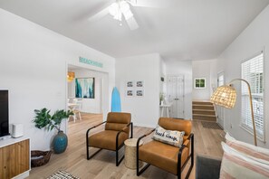 A modern living room with a sofa, armchairs, a coffee table, and a TV. There is a staircase leading to another level. - Seaglass! Folly 30 night Minimum Stay-Close to Beach & Town- (Folly Beach)
