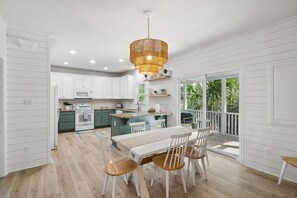 A modern kitchen with white cabinetry, a central island, and a dining area with a table and chairs. - Seaglass! Folly 30 night Minimum Stay-Close to Beach & Town- (Folly Beach)
