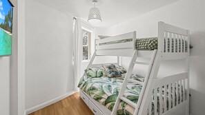 Un letto a castello con copripiumino a motivo di foglie tropicali, una finestra vista alberi e un lampadario.