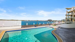 Ein Schwimmbecken mit Meerblick, eine Holzterrasse und ein weißer Zaun.