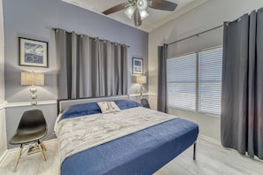 A bedroom with a bed, a ceiling fan, a chair, a window with blinds, and two wall-mounted lamps. - Historic Bungalow + Guest House • Patio & Grill (Tampa)
