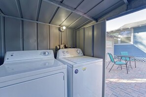 Un área de lavandería con dos lavadoras, una lámpara en el techo y un patio con sillas y una mesa.