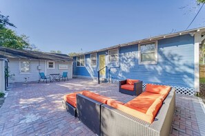 A patio with outdoor furniture, a covered area, and a blue building with windows. - Historic Bungalow + Guest House • Patio & Grill (Tampa)