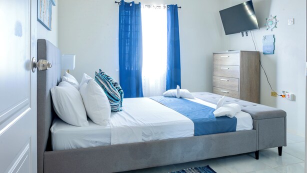 Une chambre à coucher avec un lit, une commode, un téléviseur et une fenêtre avec des rideaux.