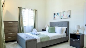Une chambre d’hôtel avec un lit, une commode, une table de chevet, une lampe et des œuvres d’art accrochées au mur.