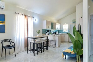 A modern kitchen with a central island, a dining area with a table and chairs, and a living space with a sofa and a large plant.