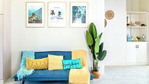 Un canapé bleu agrémenté de coussins à motifs, une plante tropicale et des tableaux encadrés accrochés au mur.