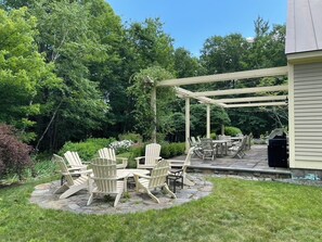 Eine Terrassenfläche mit Adirondack-Stühlen, einem Tisch und einer Pergola.