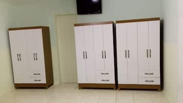 Une pièce avec deux armoires blanches, dotées d’une base et de poignées en bois, un téléviseur à écran plat fixé au mur et un sol carrelé.