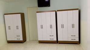 A room with two white wardrobes with wooden bases and handles, a flat-screen TV mounted on the wall, and a tiled floor.