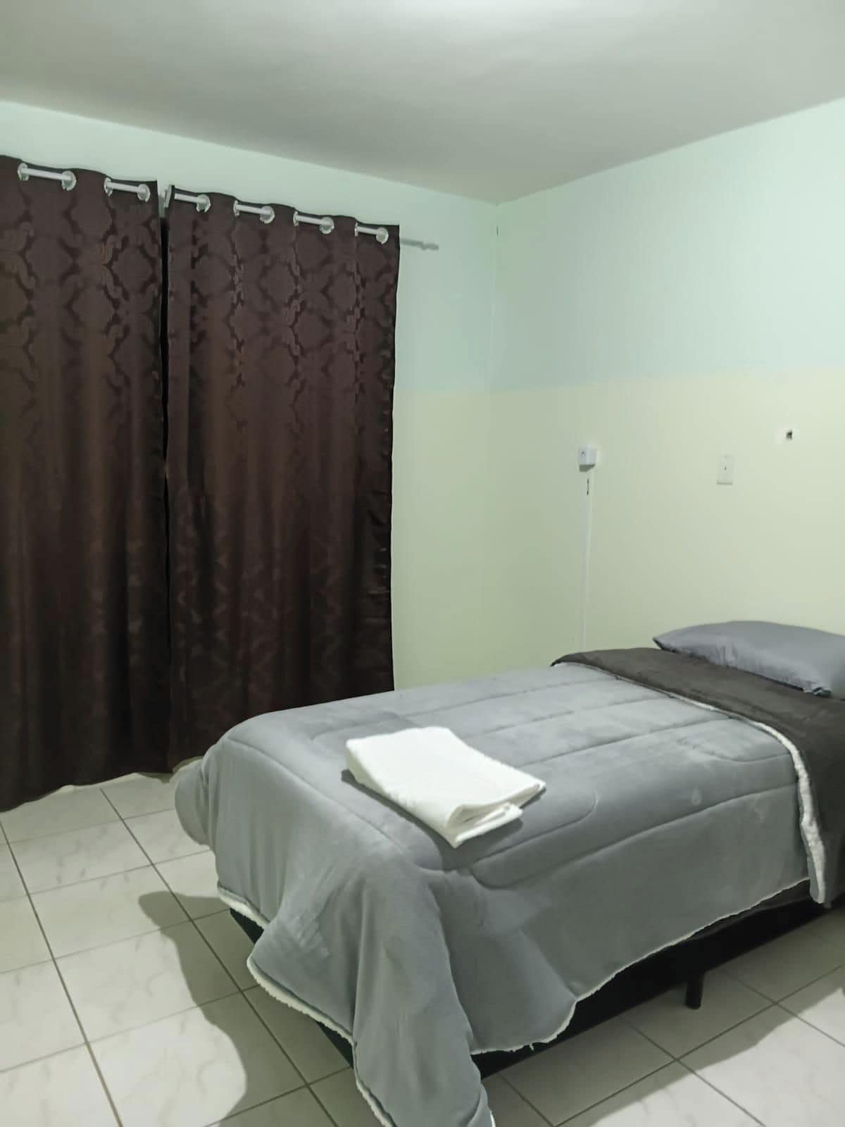 Un dormitorio con cama, cortinas y un interruptor de luz en la pared.