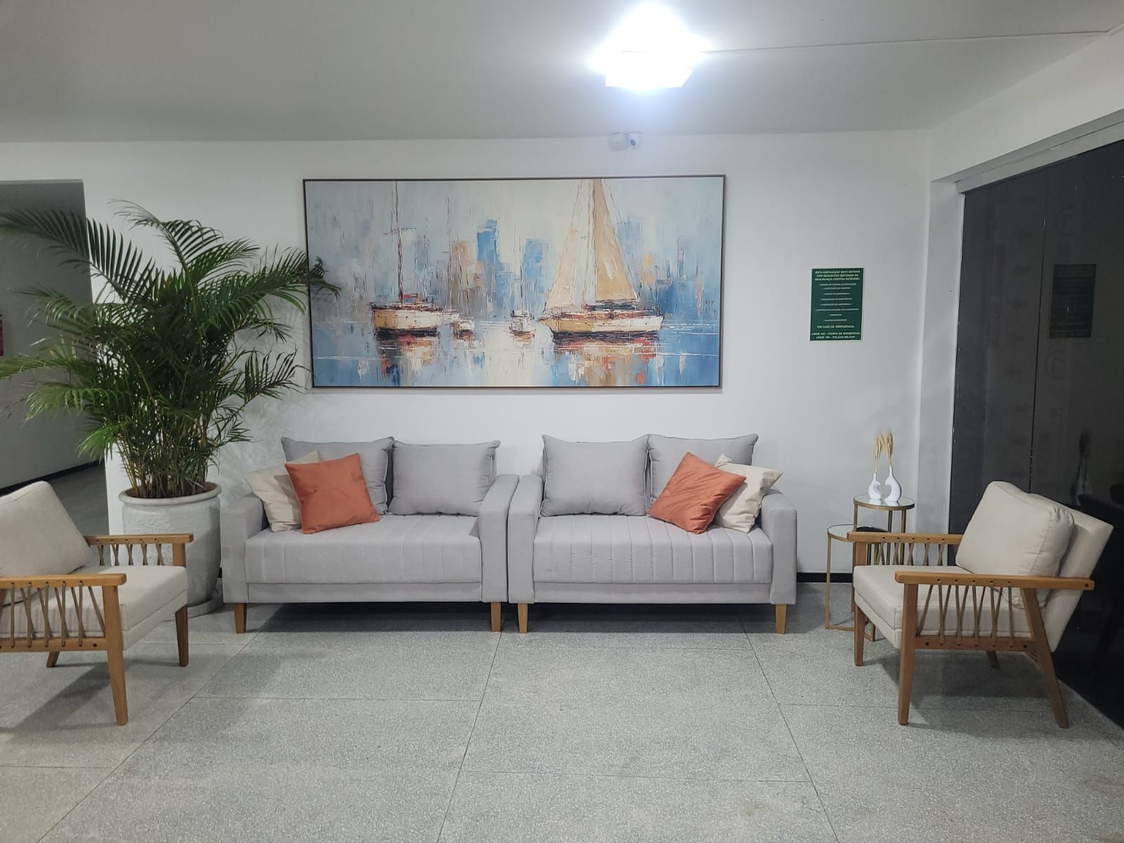 Ein Wohnzimmer mit einer Sofagarnitur, zwei Sesseln, einem großen Gemälde, einer Zimmerpflanze und einer Tür.
