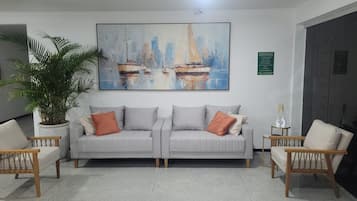 Un salon comprenant un canapé, deux fauteuils, un grand tableau, une plante en pot et une porte.