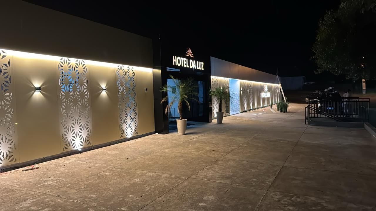 Entrada de hotel com fachada moderna, sinalização iluminada e calçada.