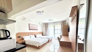 Quarto de hotel com cozinha compacta, cama, escrivaninha e uma janela grande.