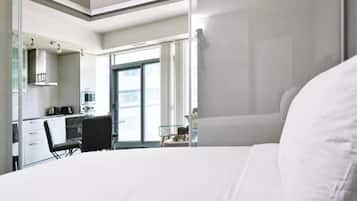 A modern hotel room with a bed, a desk, and a kitchenette.