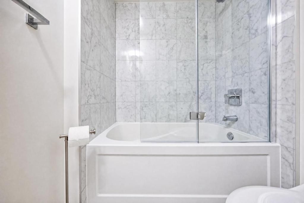 A bathroom with a glass-enclosed shower, a white bathtub, and a toilet with a paper towel holder.
