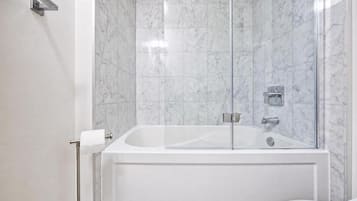A bathroom with a glass-enclosed shower, a white bathtub, and a toilet with a paper towel holder.