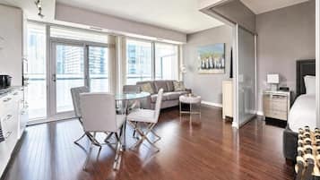 A modern living room with a glass dining table, a sofa, and a bed with a headboard.